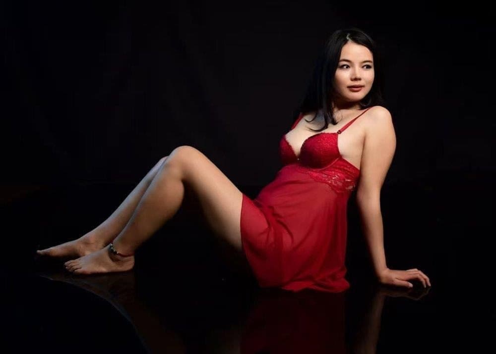 Cherry Red reclining in red against a dark studio background