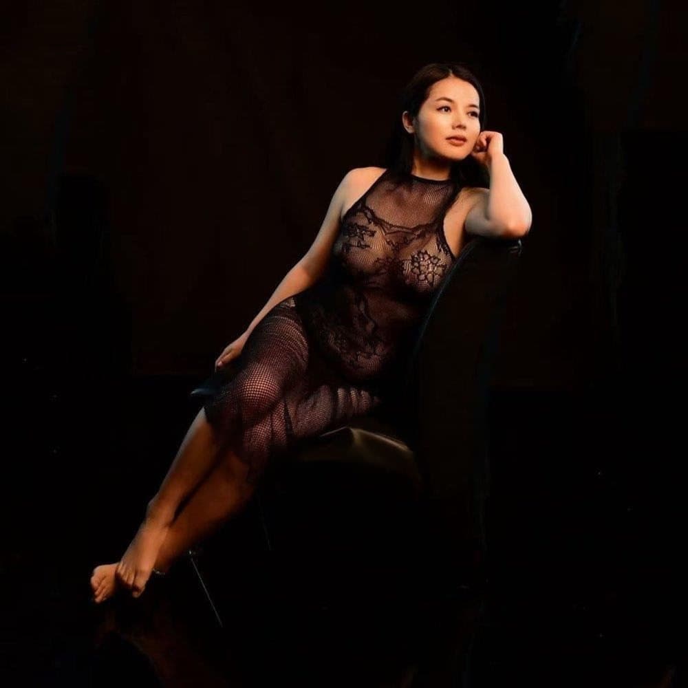 Cherry Red seated in black lace against a dark studio background